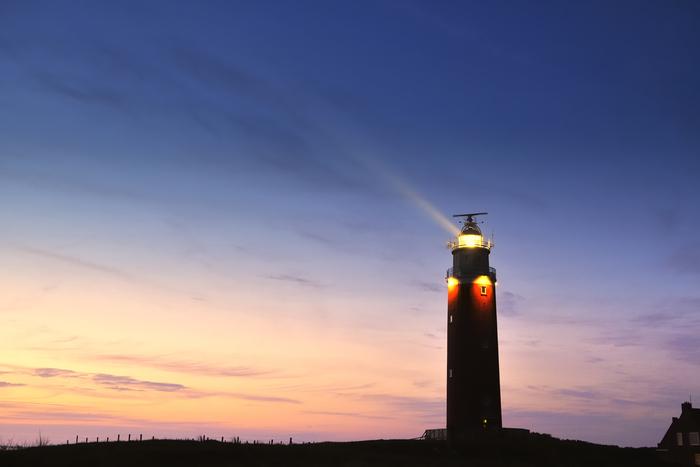A lighthouse beams light across a twilight sky A lighthouse beams light across a twilight sky, silhouetted against soft pink and deep blue hues.