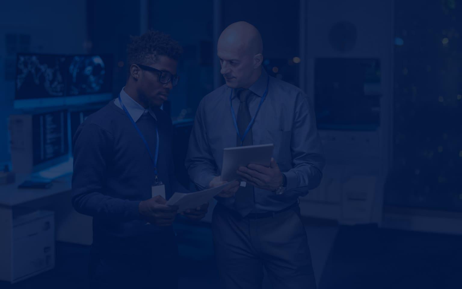 Two men in suits stand side by side, holding a tablet, symbolizing collaboration in threat exposure management.