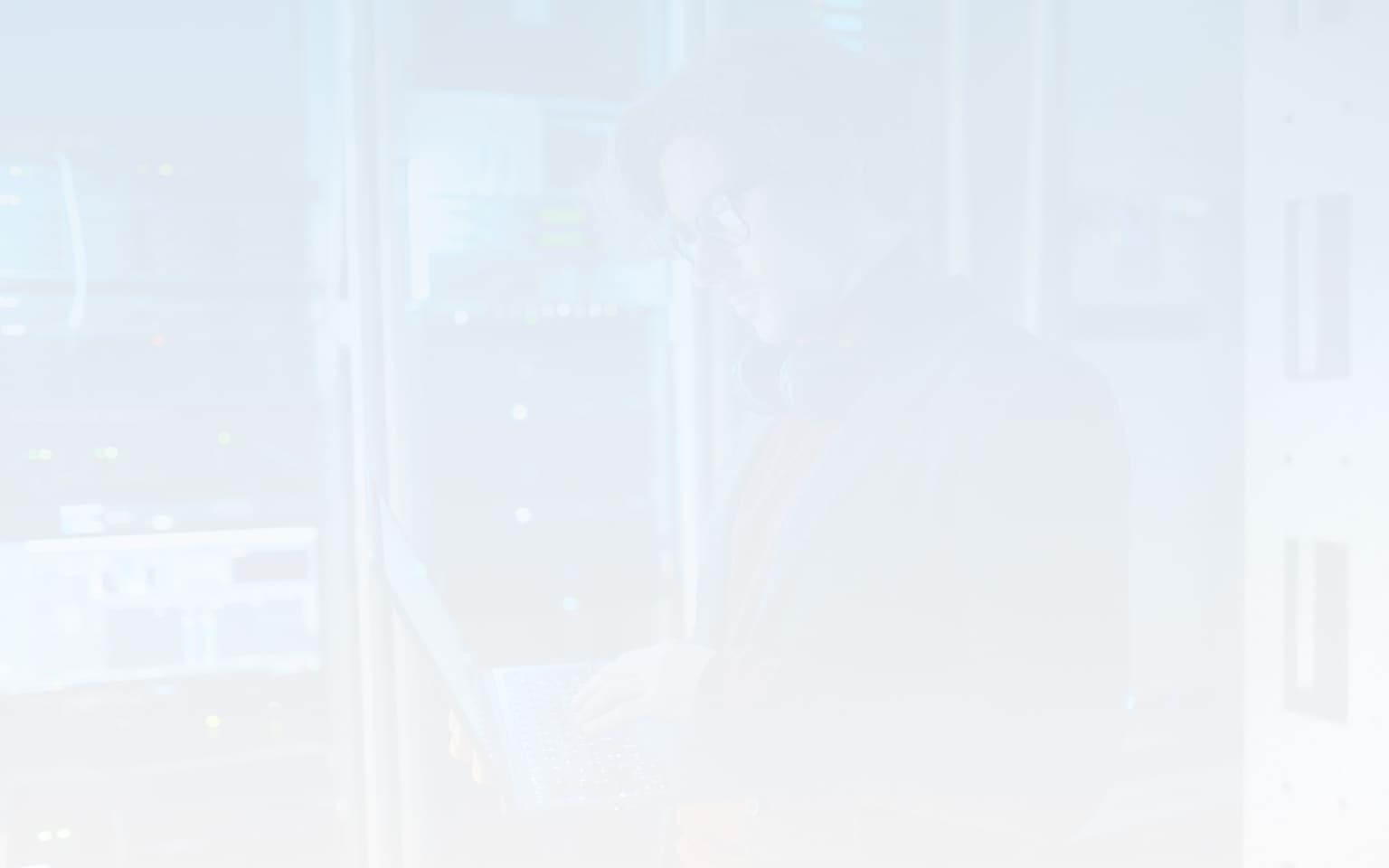 A man with glasses standing behind a server using a laptop to work on their cloud security