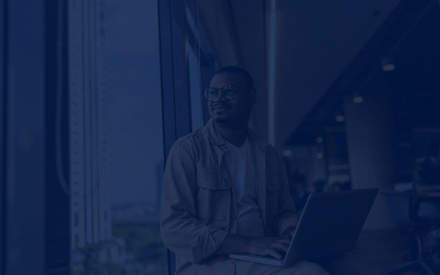 A man with glasses is seated before a laptop, set against a green backdrop, symbolizing Zscaler Cyber Academy.