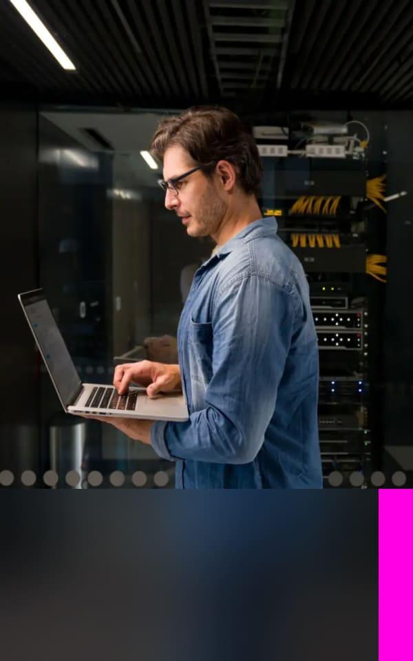 A man stands before a computer and laptop, exploring malware information and strategies to safeguard against cyber threats.