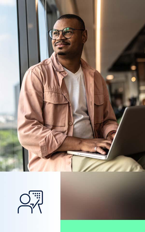 A man with glasses is seated before a laptop, set against a green backdrop, symbolizing Zscaler Cyber Academy.